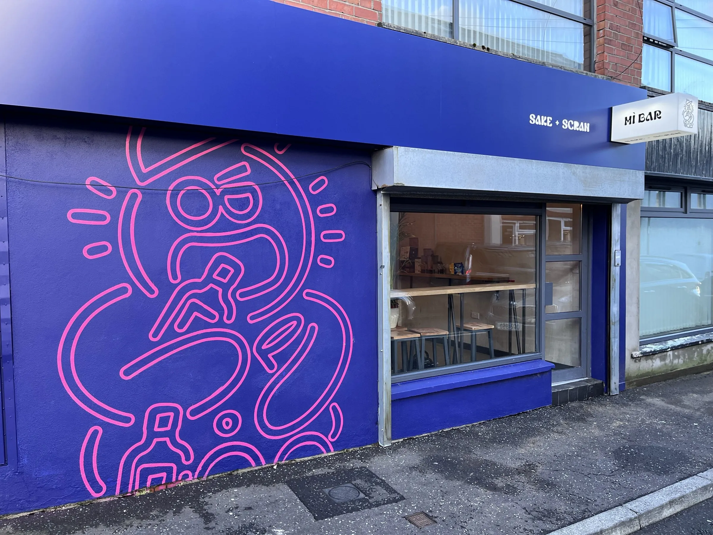 The Bánh Boy shopfront in deep blue, with a large pink line-drawn face painted across the side wall.