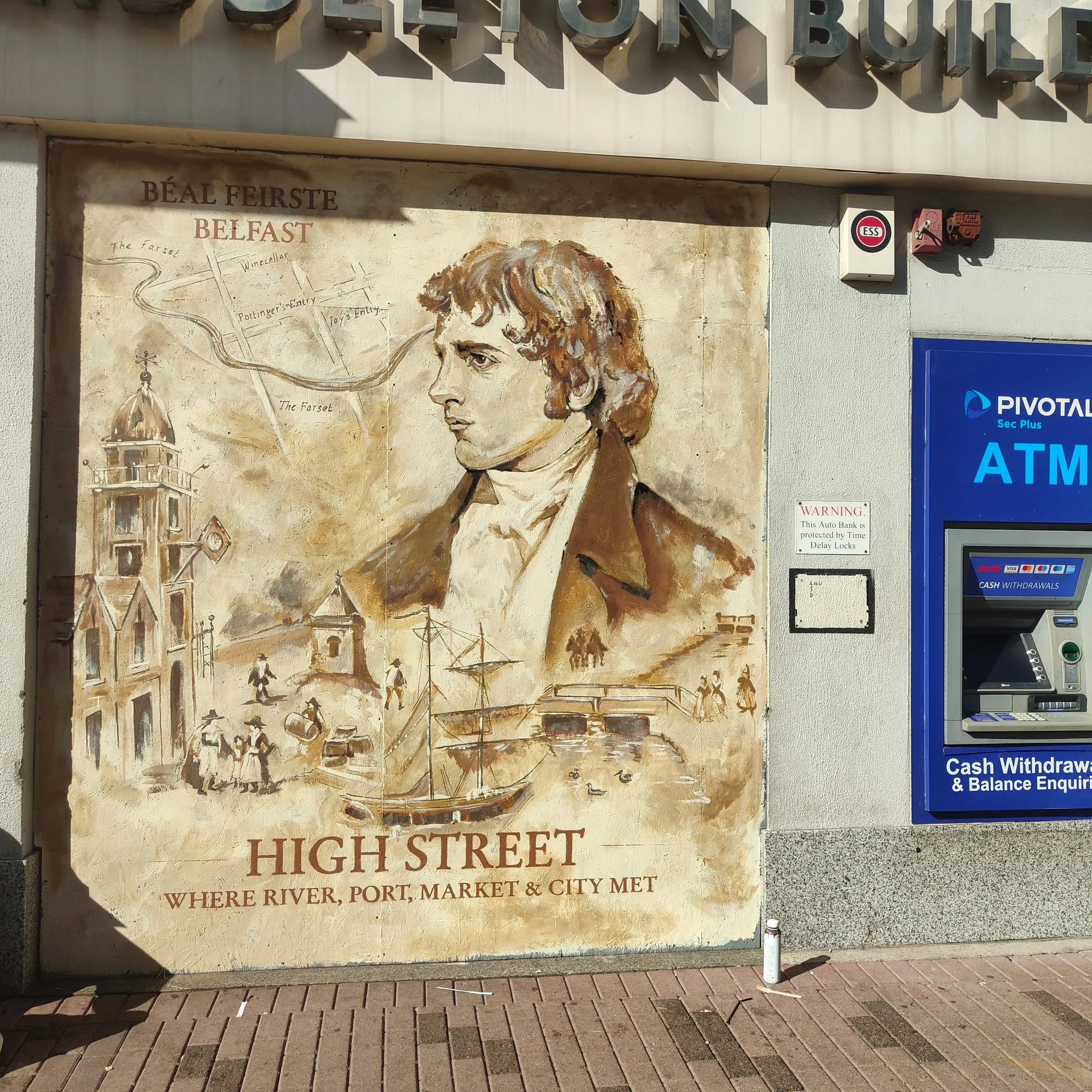A sepia mural on the Middleton Building of a young man in a high-collared coat above old Belfast’s quays and ships, titled “High Street, where river, port, market & city met”.