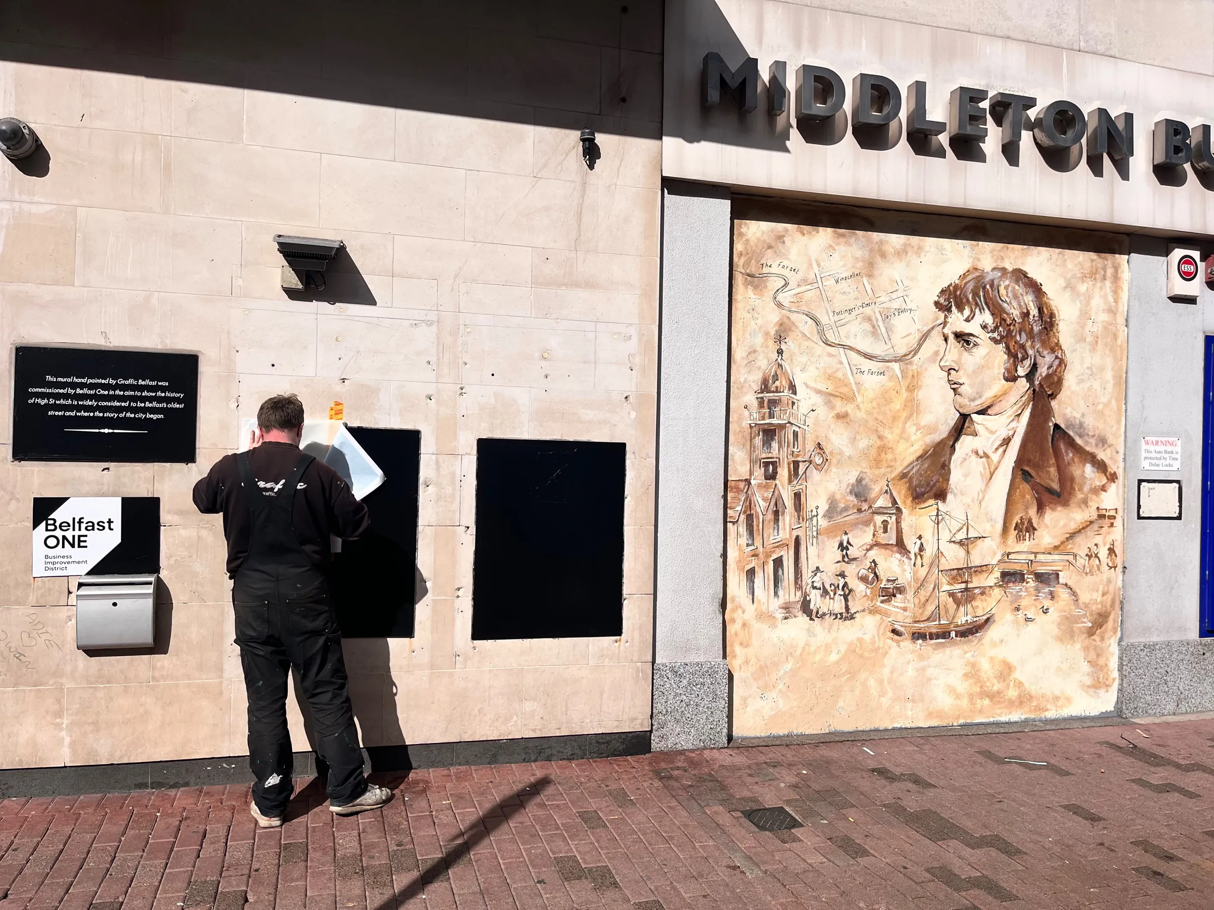 A painter fixing information panels to the wall beside the finished High Street mural.