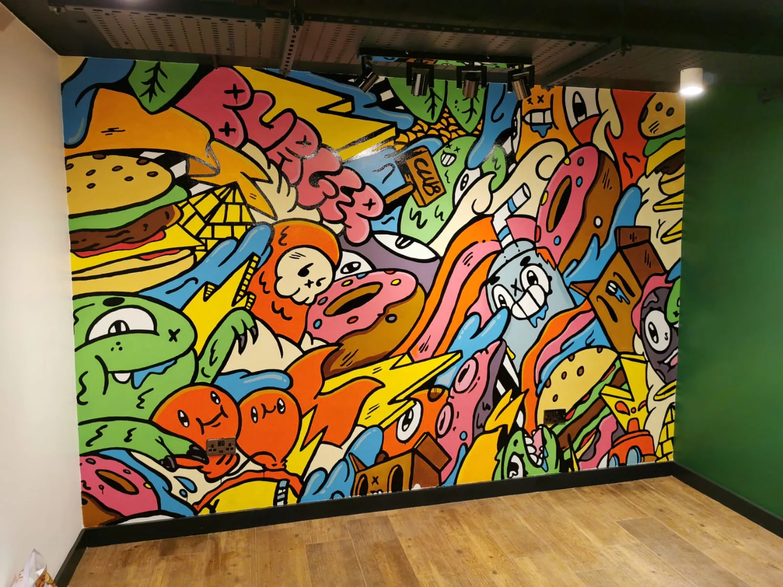 An interior wall at The Burger Club covered edge to edge with a bright cartoon mural of burgers, fries, drinks and characters.