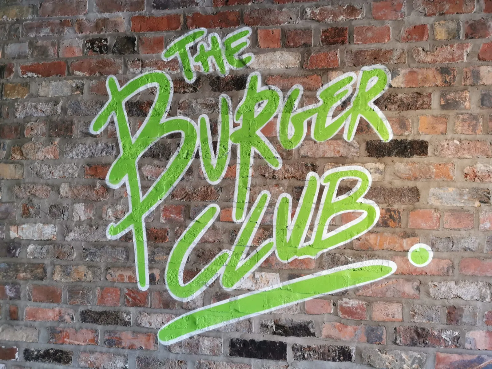 A wider view of the green “The Burger Club” script painted across the brick wall.