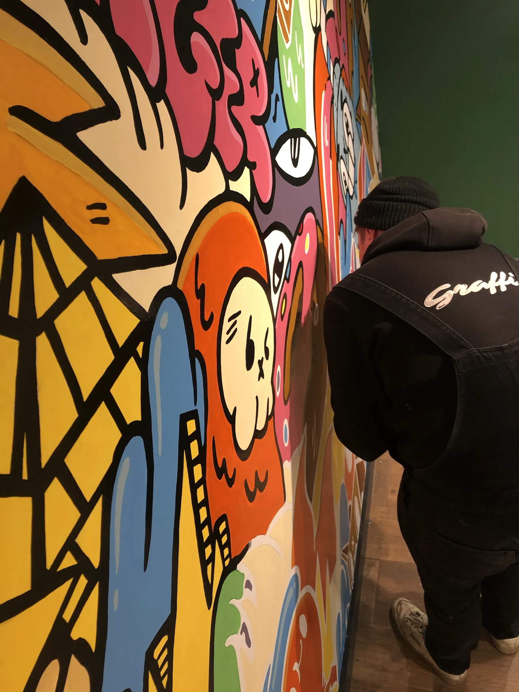 A Graffic painter at work on the Burger Club’s cartoon mural, its bold characters outlined in black.