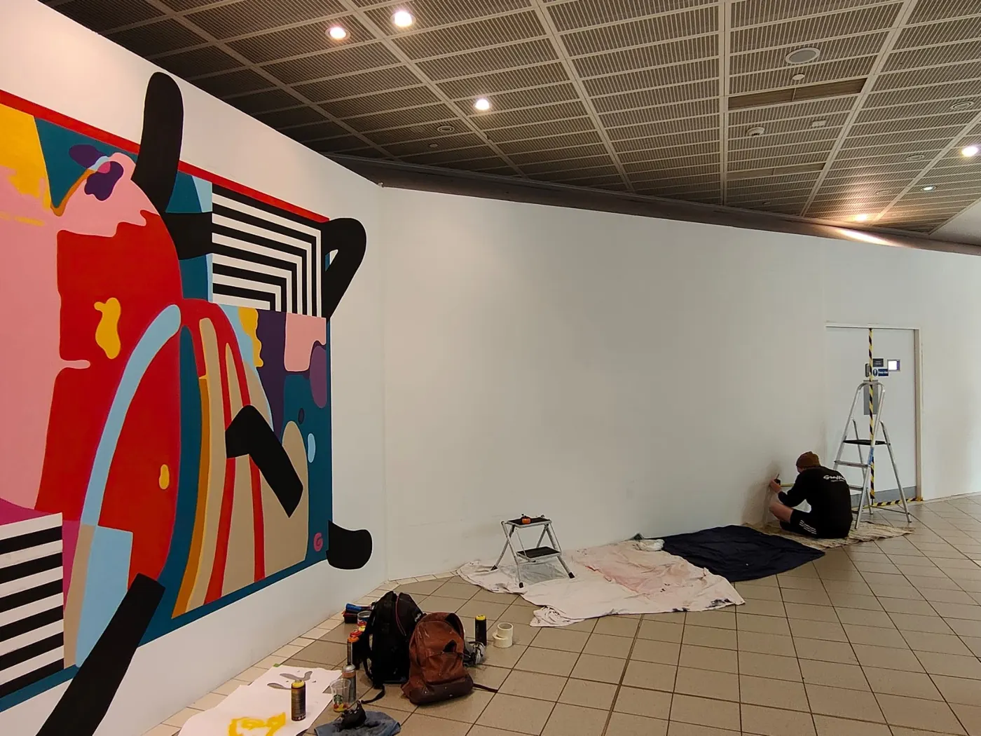 One of the six CastleCourt artworks part-finished — the abstract panel complete on the left, a painter working at the far end of the hoarding.