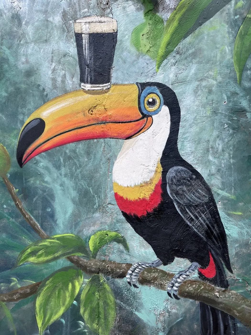 A hand-painted toucan balancing a pint of Guinness on its beak, perched on a branch against a misty rainforest background.