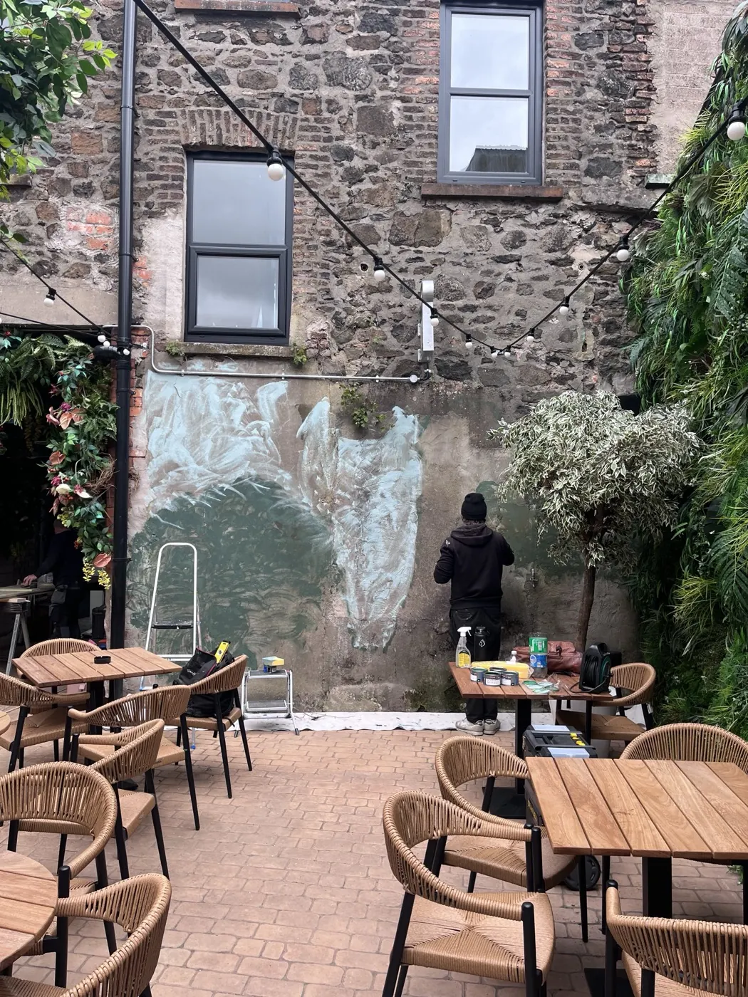 A painter blocking in the pale underpainting of the rainforest mural on the bar’s old stone wall.
