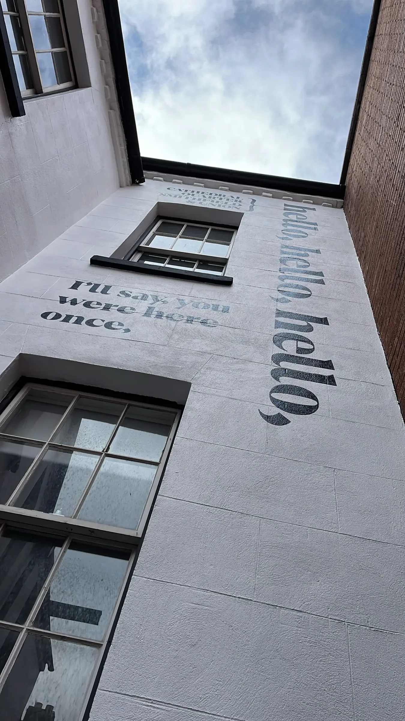 Looking up at the black “hello, hello” lettering running along the white wall in Exchange Place.