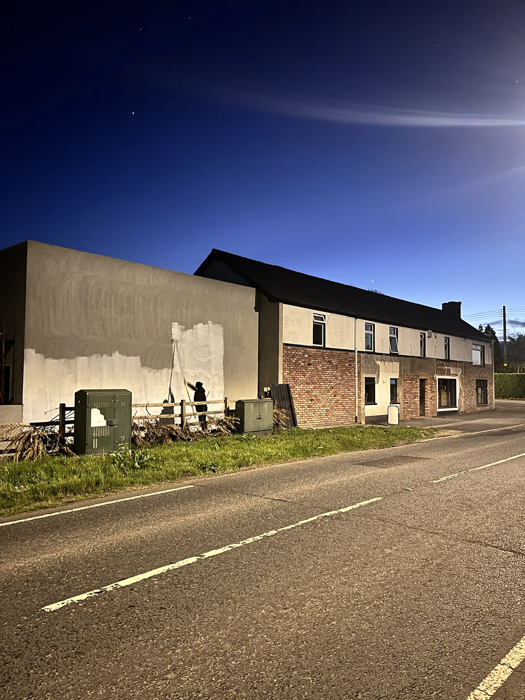 The Five Corners Inn at dusk, its gable still blank, seen from the road.