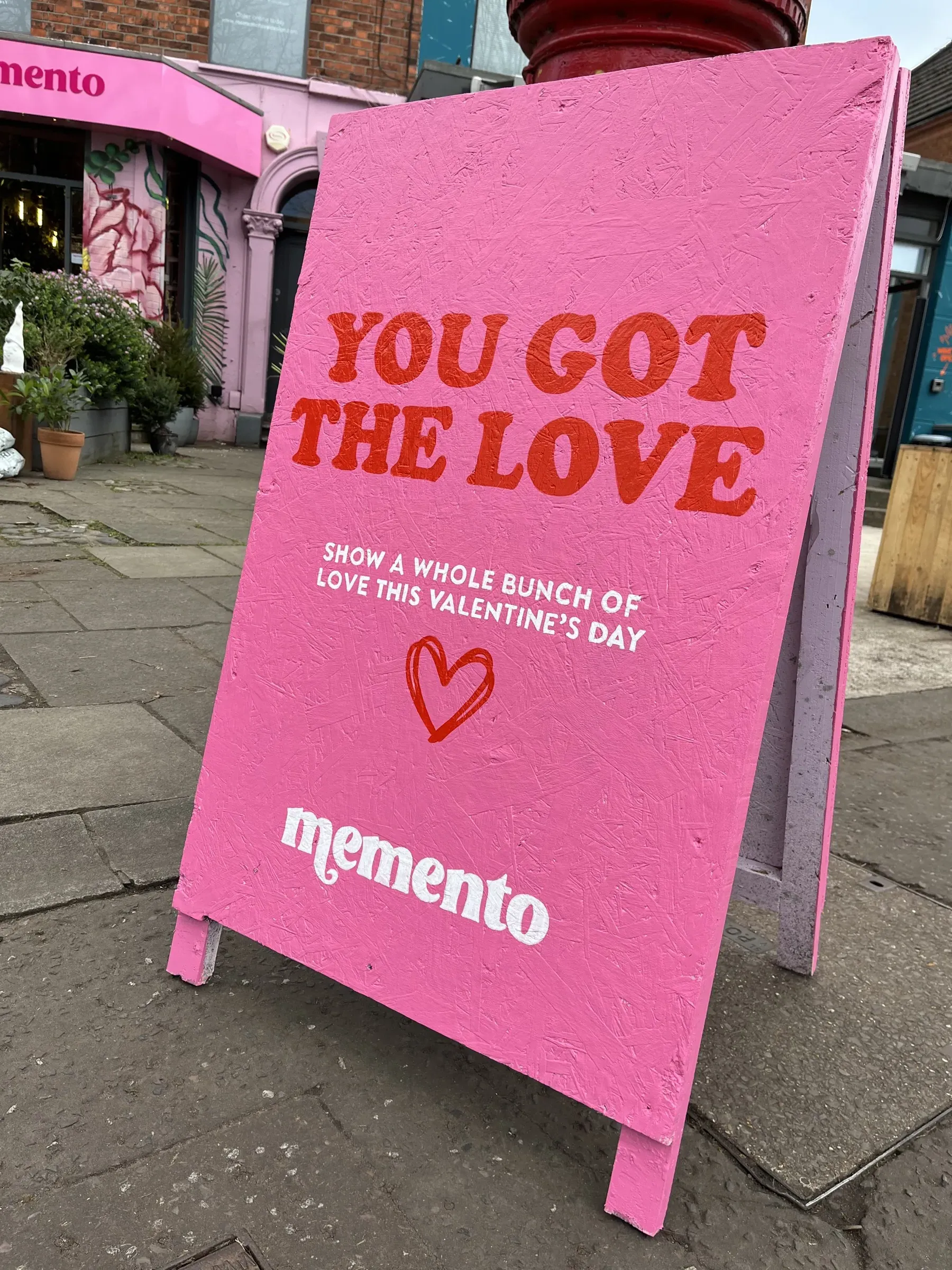 A pink A-board for Memento, hand-painted with “You got the love” in red lettering and a small red heart for Valentine’s Day.
