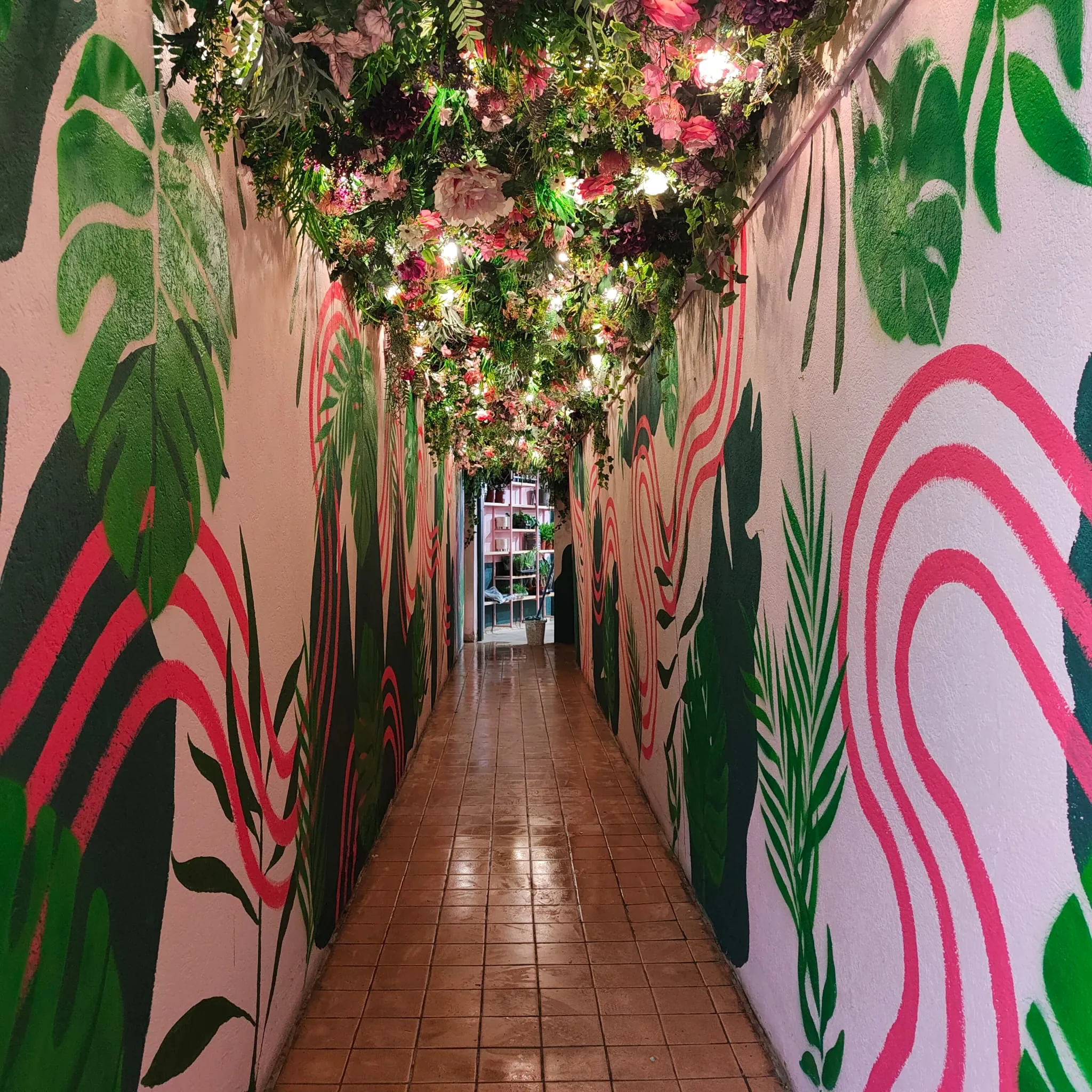A long pink corridor painted with tropical leaves and pink swirls beneath a ceiling of hanging flowers.