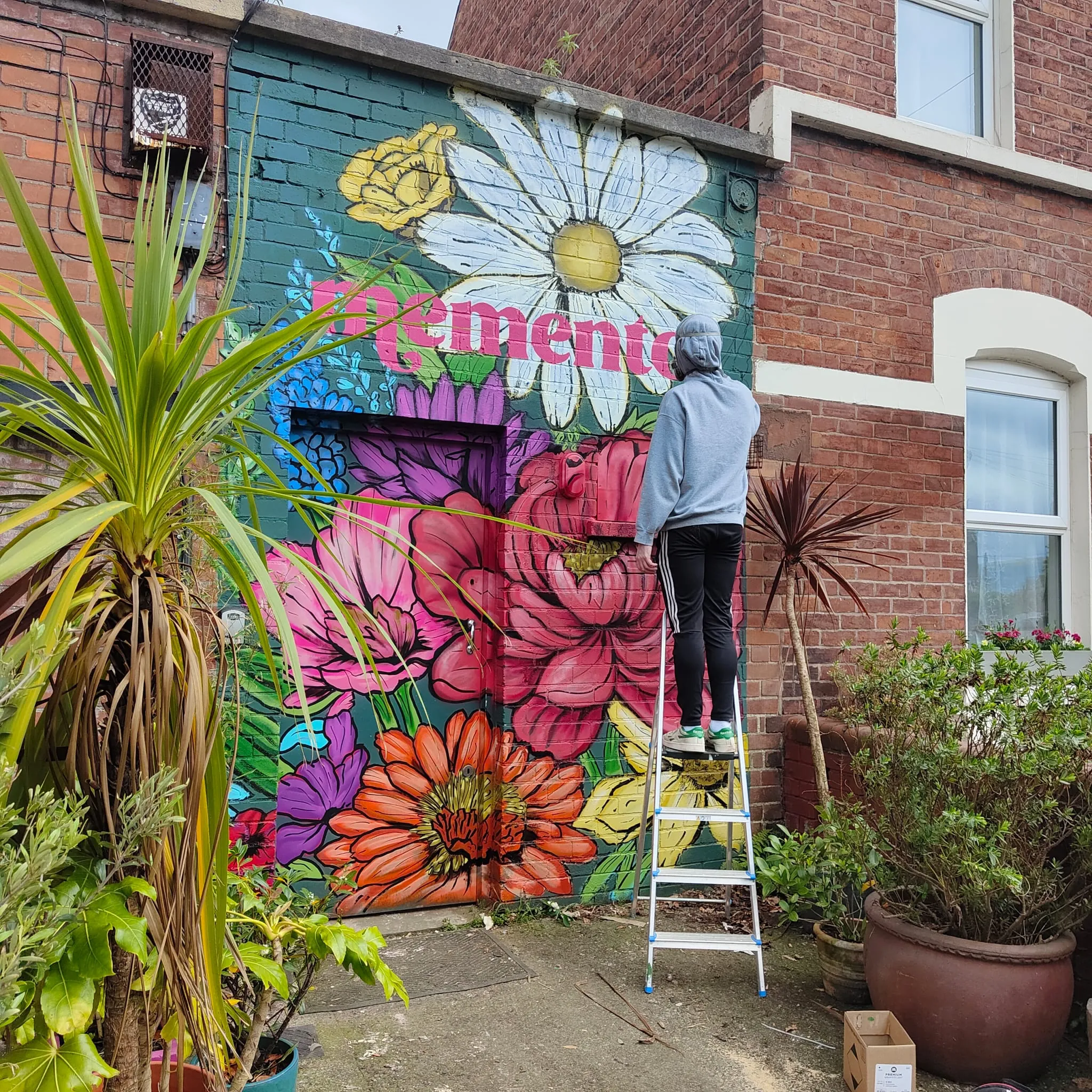 A painter on a stepladder finishing the Memento flower mural.