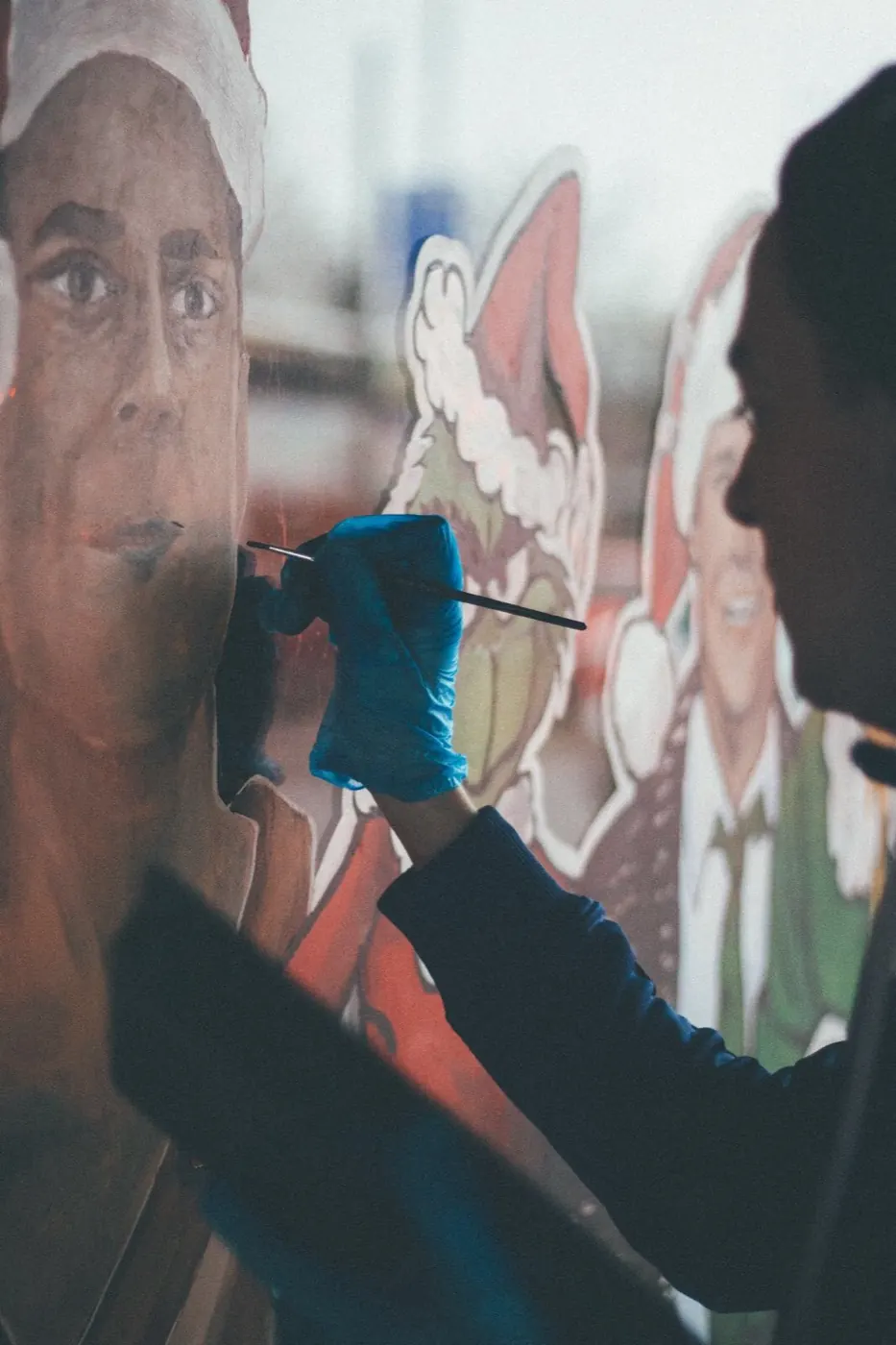 A close-up of a gloved hand painting a detailed portrait onto glass with a fine brush.