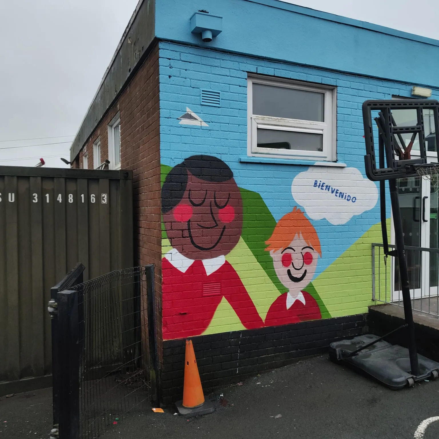 Two smiling cartoon schoolchildren in red jumpers painted on the side of a blue classroom block.