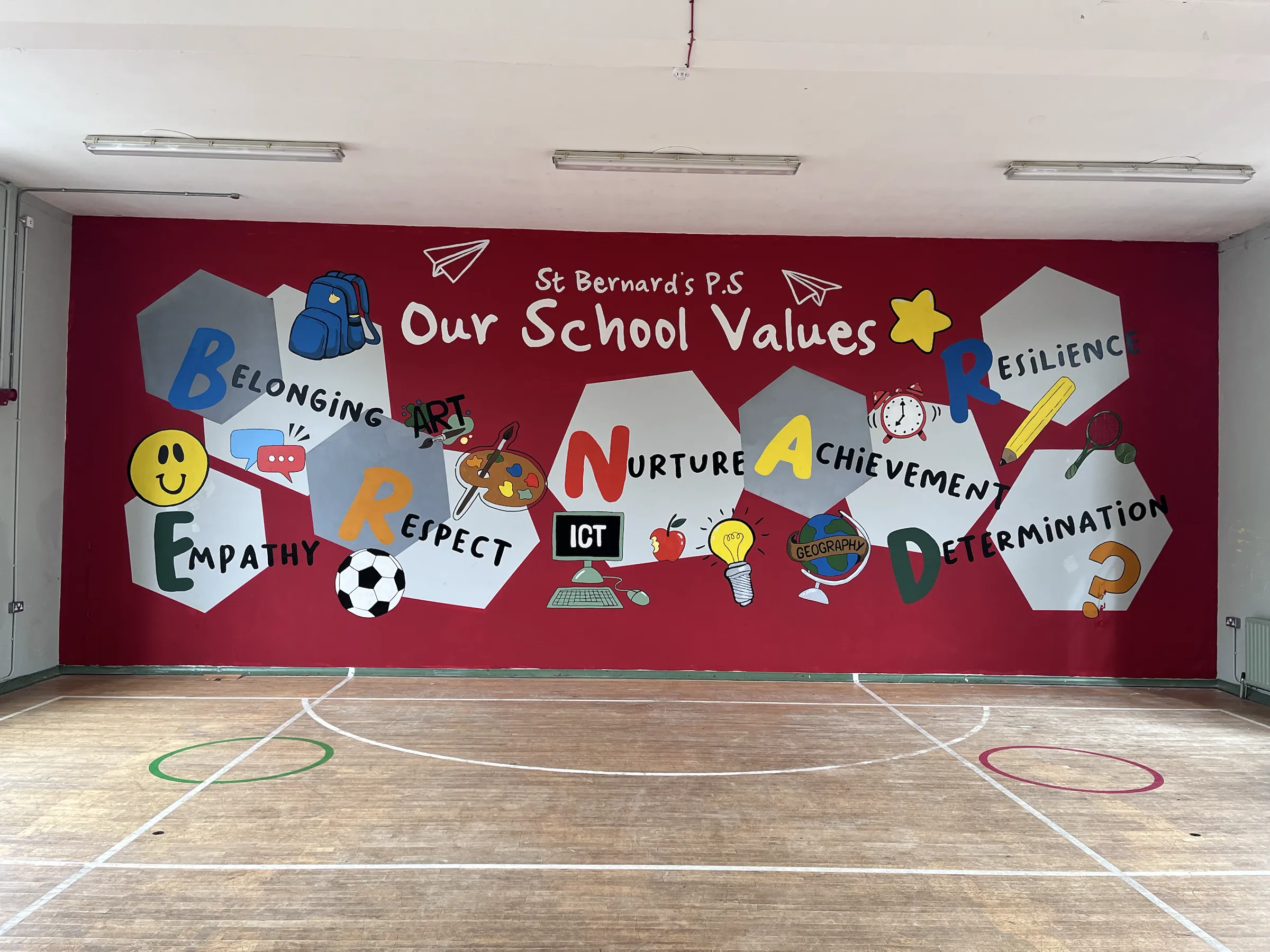 The school hall’s end wall painted red with “Our School Values” — Belonging, Nurture, Achievement, Resilience, Respect, Empathy and Determination — on white hexagons.