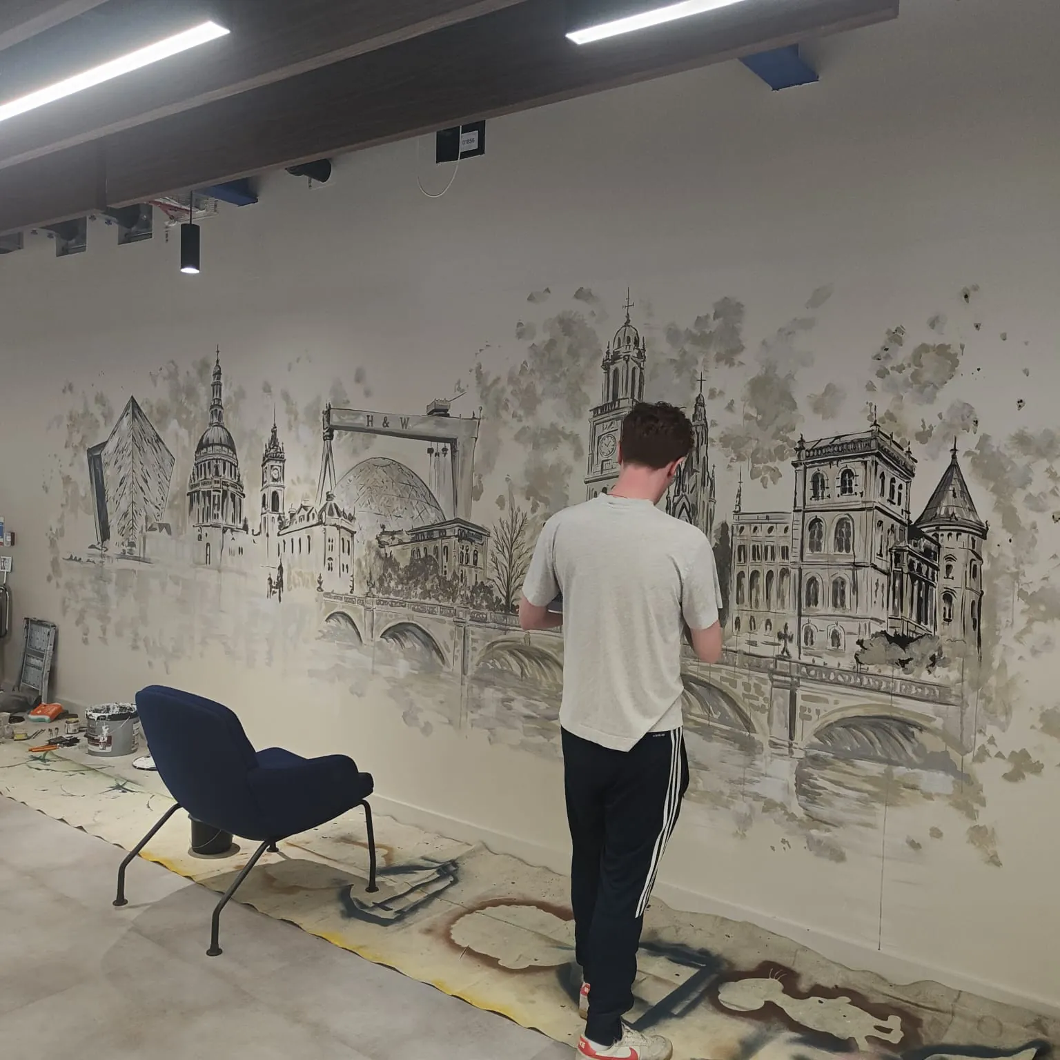 A painter adding detail to the skyline mural, a blue armchair beside the dust sheets.