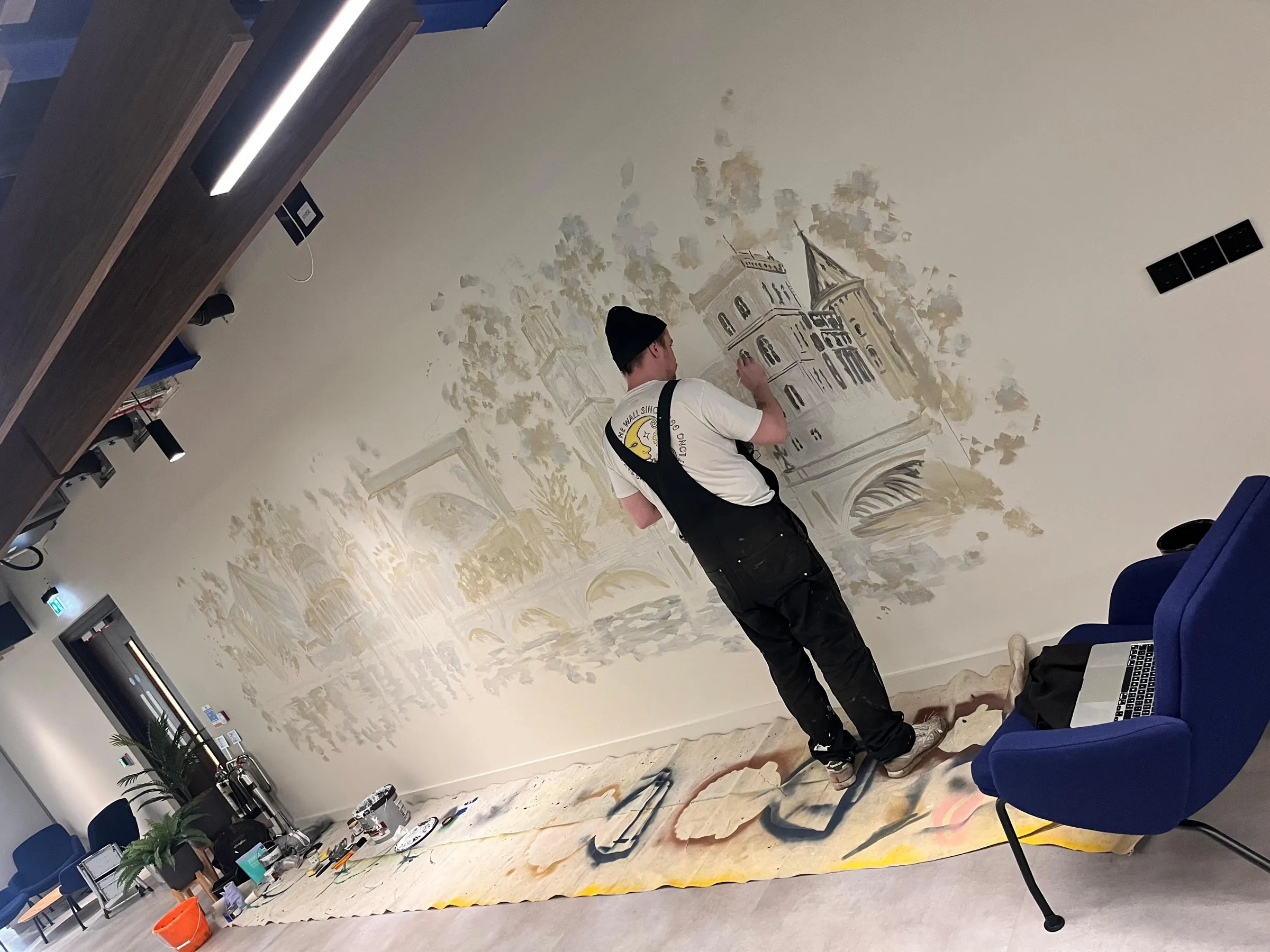 A painter in dungarees adding detail to a building in the skyline mural.