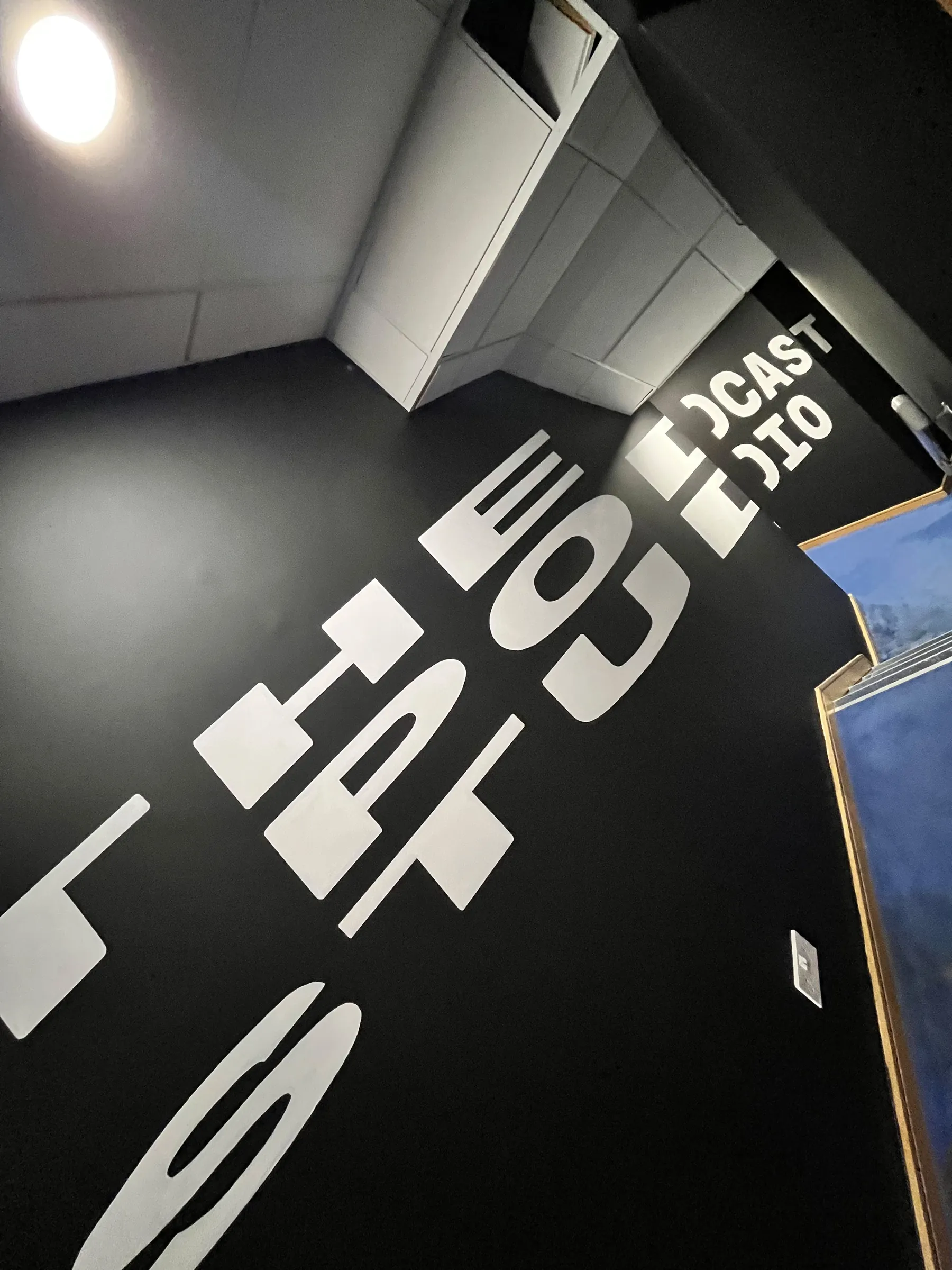 A low angle along the black wall, the white “The Podcast Studio” lettering stretching away.