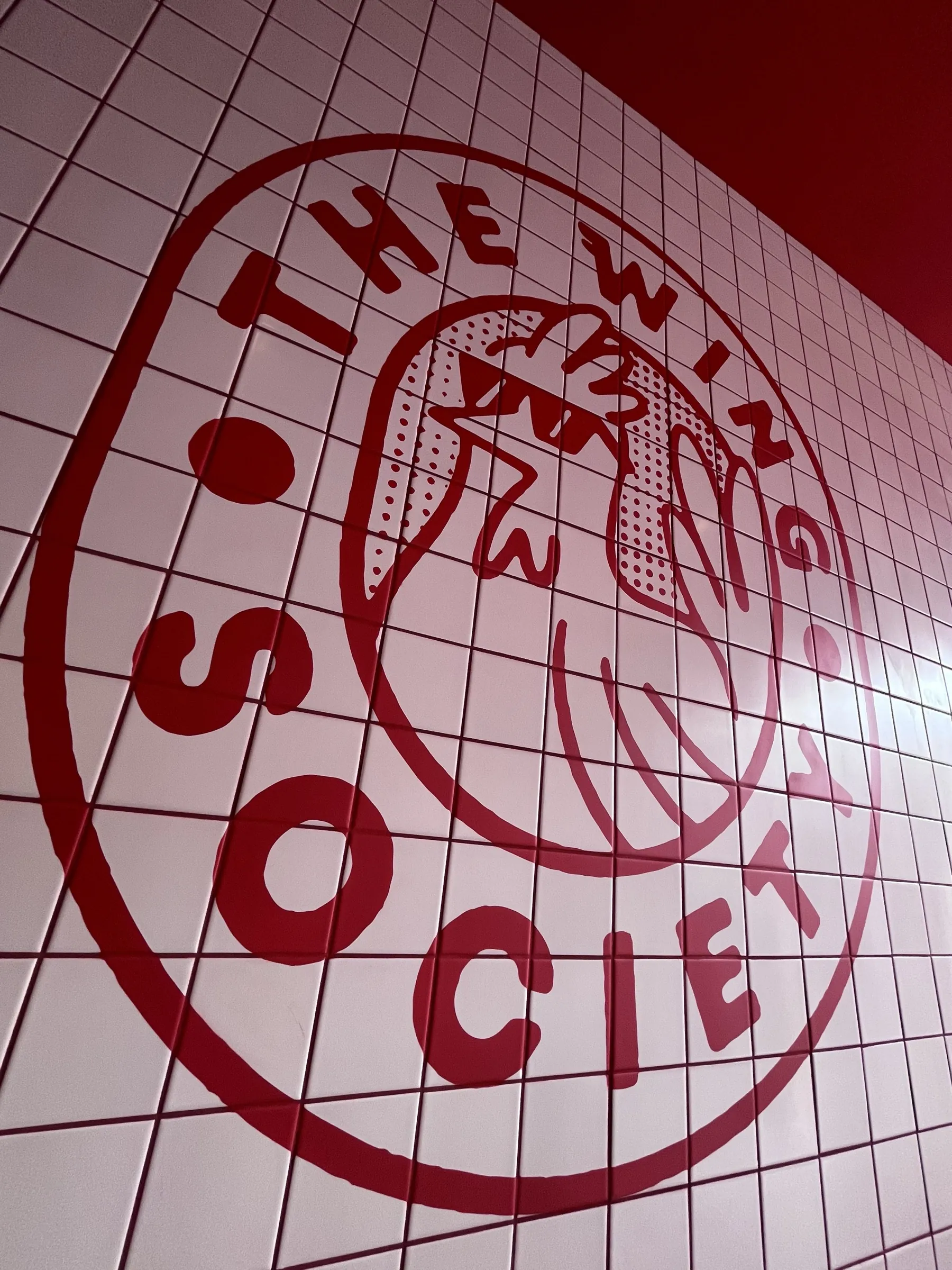 The Wing Society’s circular logo hand-painted in red across white tiling, with a chicken wing at its centre.
